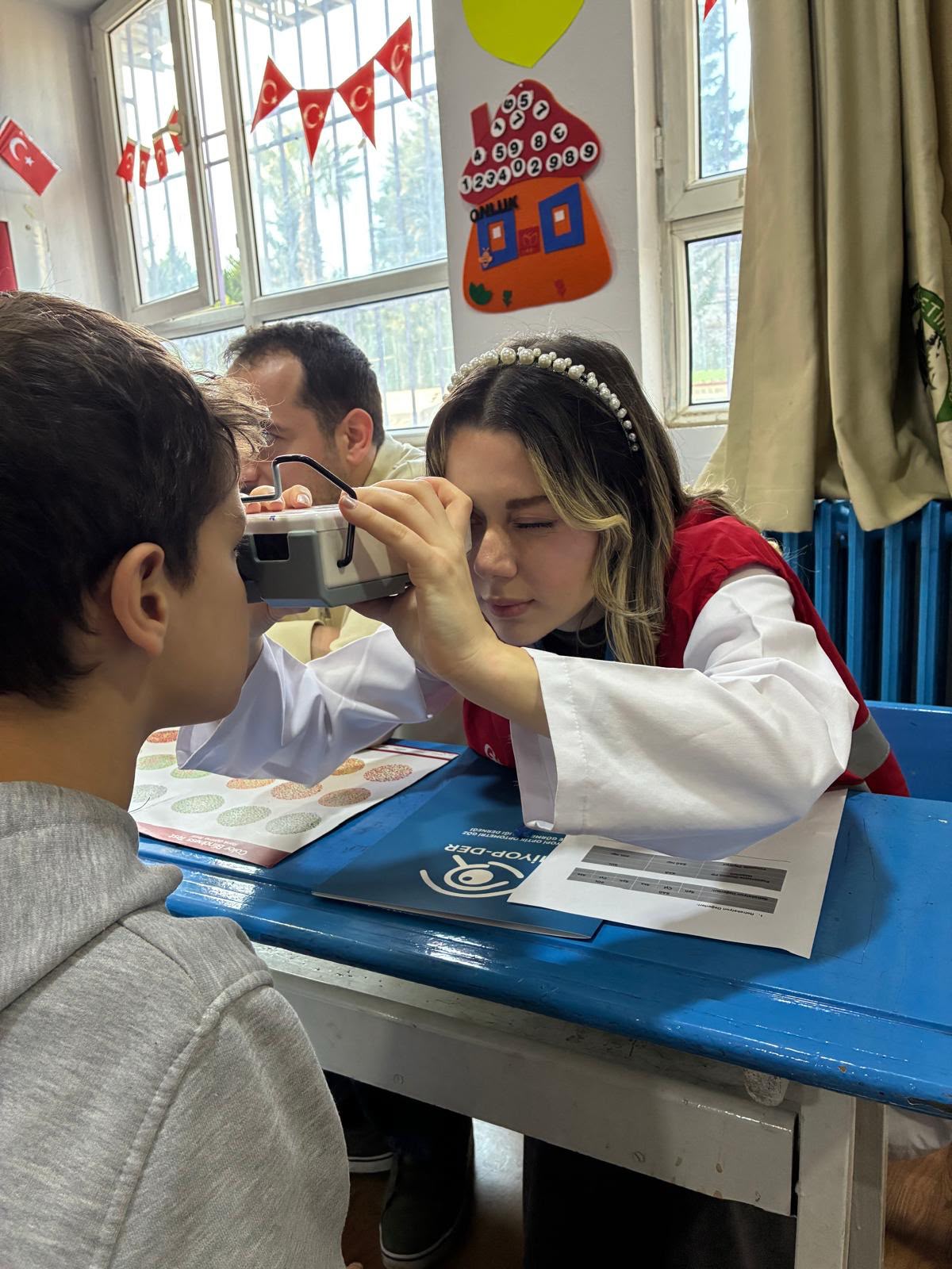 Kızılay gönüllüsü bir çocuğun gözünü tarama cihazıyla inceliyor