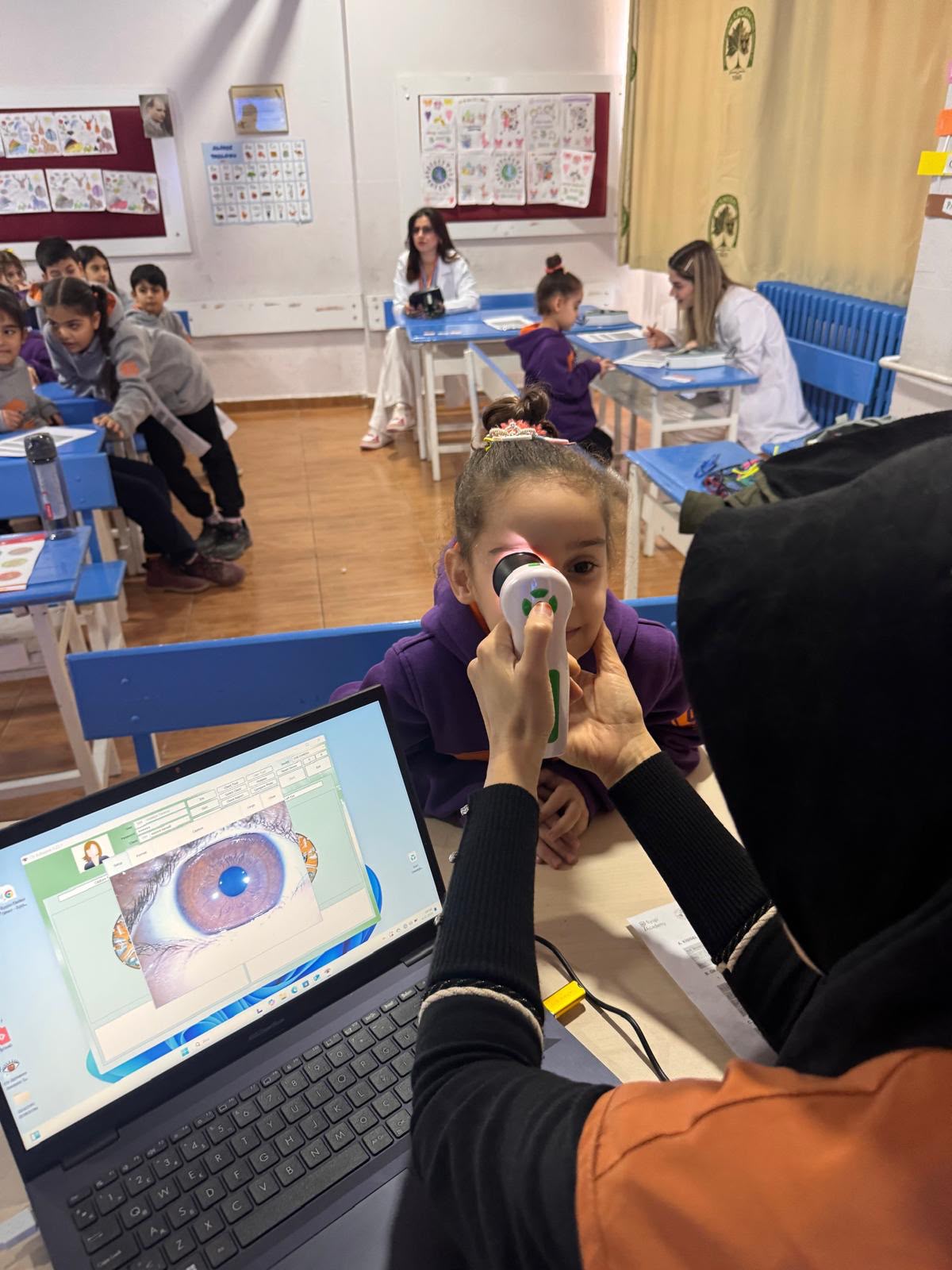 Bir sınıfta el tipi cihazla gözü incelenen bir çocuk